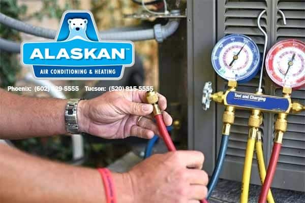 hands using testing and charging gauges on AC unit with Alaskan Air Conditioning and Heating logo and contact phone numbers in top left corner